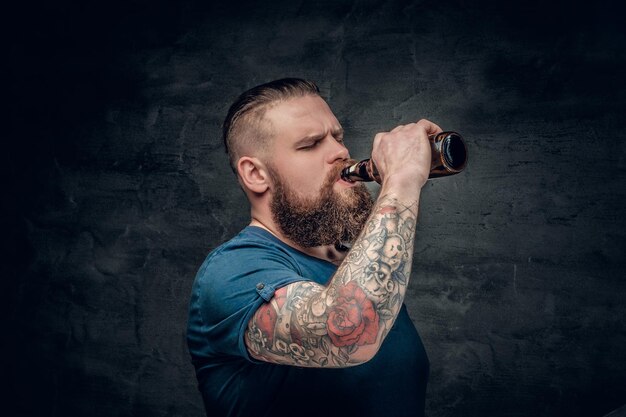 De gros hommes barbus tatoués sur le bras boivent de la bière dans une bouteille.