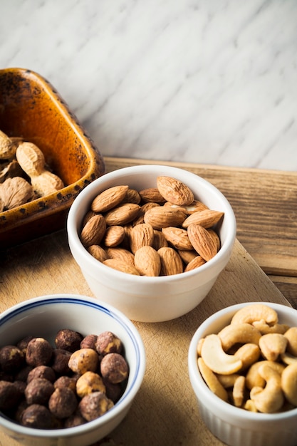 Photo gratuite gros plan d'amande; noisette; noix de cajou et cacahuètes dans un bol sur une planche à découper