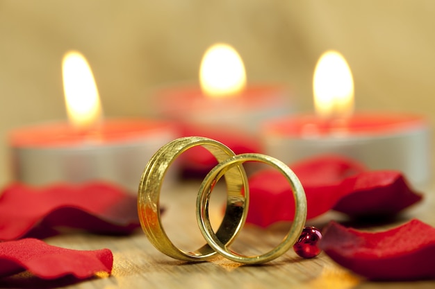 Gros plan des anneaux de mariage avec un fond de belles roses rouges et bougies sur la table