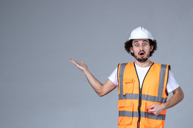 Gros plan d'un architecte masculin surpris en gilet d'avertissement avec casque de sécurité et pointant quelque chose sur le mur de la vague grise