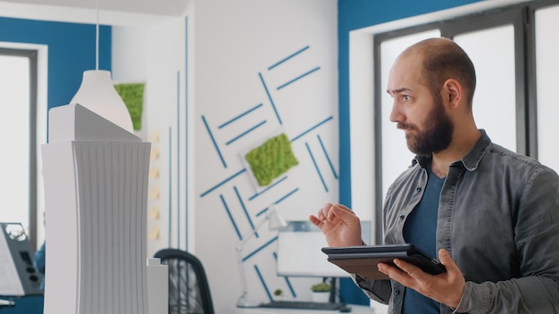 Photo gratuite gros plan sur un architecte utilisant une tablette numérique et un modèle de bâtiment pour travailler sur la conception de la construction. ingénieur homme travaillant avec un appareil pour planifier l'aménagement de la propriété pour le projet de développement architectural.