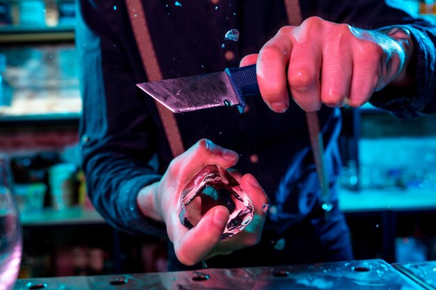 Gros plan sur un barman écrasant un gros morceau de glace sur le comptoir du bar avec un équipement de bar spécial dessus pour un cocktail