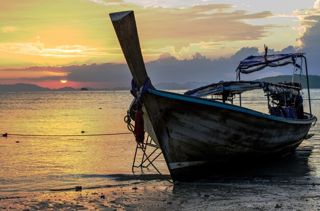 Gros plan d'un bateau en bois sur la plage entourée par la mer sous un ciel nuageux pendant le coucher du soleil