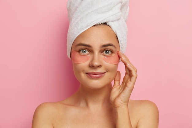 Photo gratuite gros plan d'un beau modèle féminin européen fait des procédures de spa après la douche, applique des patchs de collagène sous les yeux, a un traitement anti-âge, se tient à l'intérieur