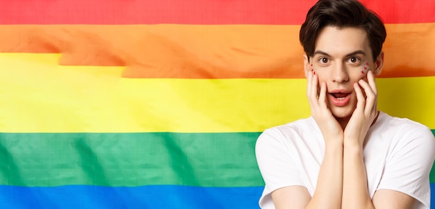 Gros plan d'un bel homme gay brune en t-shirt blanc avec un maquillage scintillant qui a l'air amusé devant la caméra t