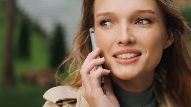 Gros plan sur une belle étudiante qui parle avec son meilleur ami au téléphone tout en se reposant dans le parc