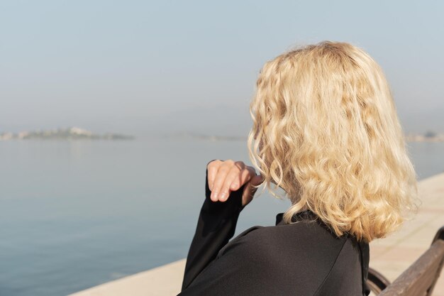 Gros plan sur une belle femme blonde adulte assise sur un banc et regardant la silhouette de la mer et du ciel bleu d'un espace de femme pour l'idée de texte pour le fond