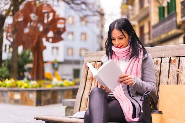 Gros plan d'une belle femme caucasienne assise sur un banc et lisant un livre dans un parc public