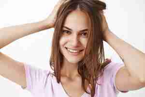 Photo gratuite gros plan d'une belle femme féminine sûre d'elle-même, touchant la coupe de cheveux et souriant joyeusement se sentant jolie se débarrasser de l'acné sur un mur gris