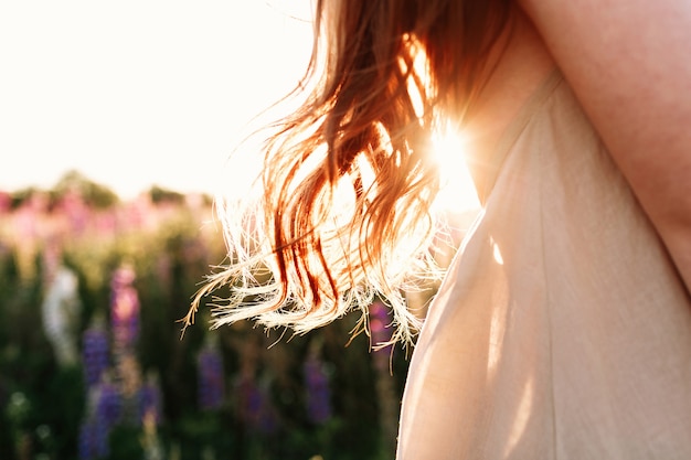 gros plan de belle femme mèche de cheveux sur fond de coucher de soleil dans le champ de la fleur.