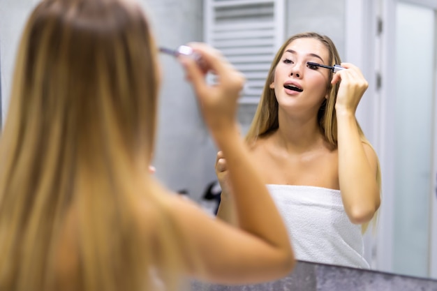 Gros plan d'une belle jeune femme appliquant du mascara dans la salle de bain à la maison