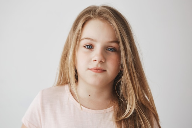 Gros plan de la belle petite fille blonde aux cheveux longs clairs et aux yeux bleu vif. Enfant avec une expression détendue