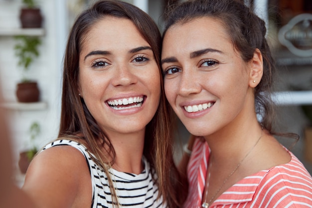 Gros plan de belles femmes avec de larges sourires, posent ensemble pour selfie, ont des expressions ravies. Des amies proches se photographient, ont une apparence attrayante et des relations sincères