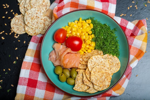 Photo gratuite gros plan d'un bol de salade avec du saumon, des craquelins et des légumes sur une serviette sur la table