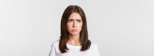 Gros plan de bouderie bouleversée jolie fille regardant le coin supérieur gauche avec jalousie debout triste sur fond blanc