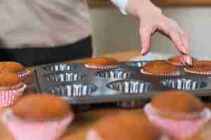 Photo gratuite gros plan de la boulangère retirant le cupcake du plateau à muffins