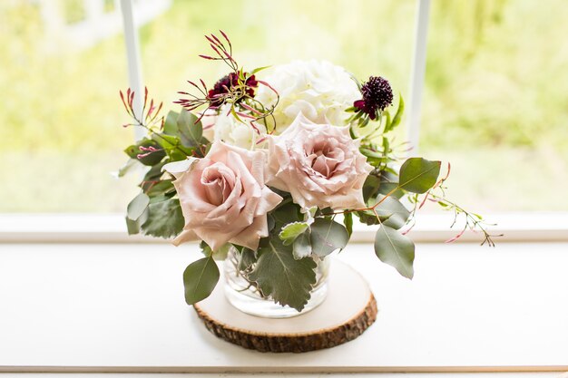 Gros plan d'un bouquet de roses dans un vase près d'une fenêtre sous la lumière du soleil