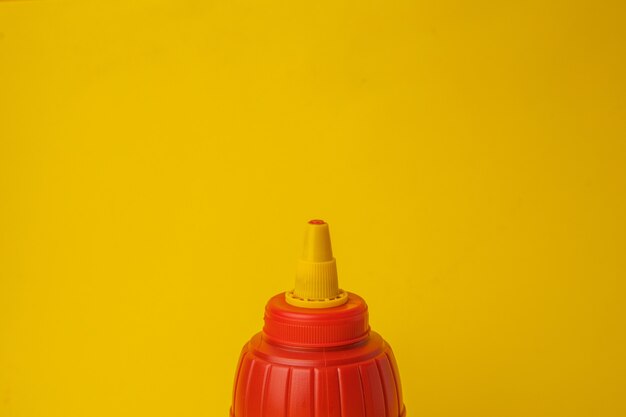 Gros plan d'une bouteille de ketchup rouge sur un mur jaune