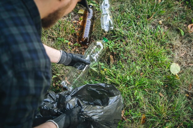 Gros plan sur une bouteille en plastique dans une main masculine nettoyant la nature