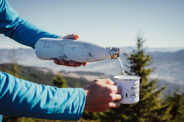 Gros plan sur les bras d'un homme mettant de l'eau d'une bouteille dans une tasse blanche