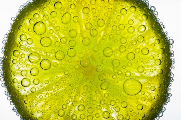 Gros plan de bulles d&#39;air couvrant une tranche de citron vert citronnée flottant dans l&#39;eau