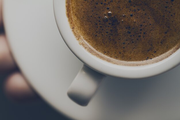 Gros plan d&#39;un café expresso savoureux avec de la mousse savoureuse dans une petite tasse en céramique. Main mâle tenant une boisson chaude chaude.