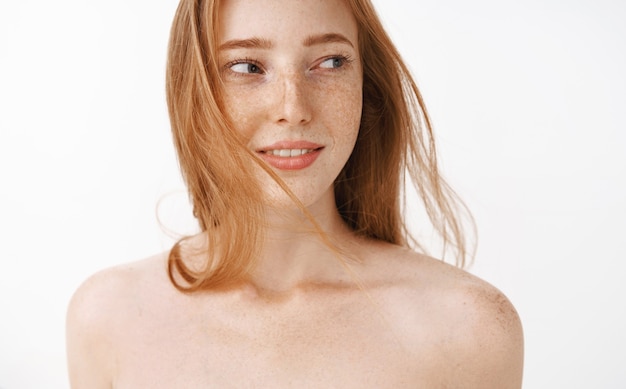 Gros plan d'une charmante femme rousse sensuelle et féminine avec des taches de rousseur posant nue étant tendre et douce tournant à droite en regardant flirty et ravi debout