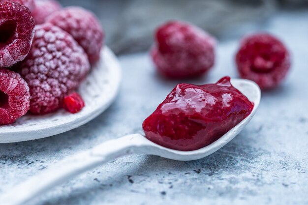 Gros plan de confiture de framboises avec des framboises congelées en arrière-plan