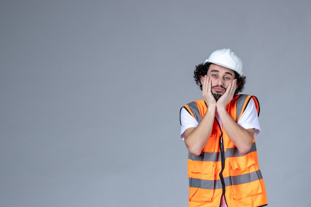 Gros plan sur un constructeur masculin pensant dans un gilet d'avertissement avec un casque de sécurité sur un mur de vague grise