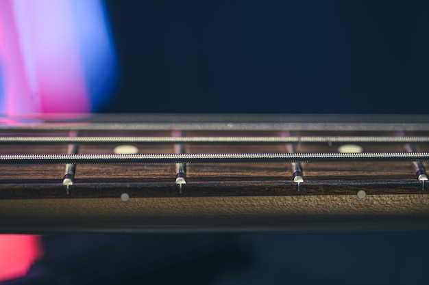 Gros plan des cordes sur le manche d'une guitare basse sur un fond sombre flou.