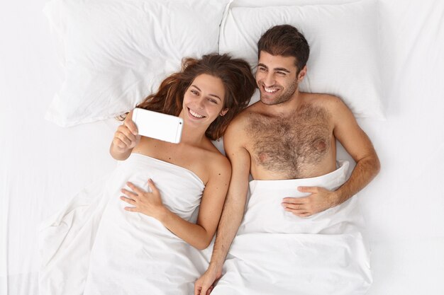 Gros plan sur couple allongé dans son lit sous une couverture blanche