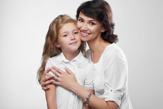 Gros plan d'un couple de famille merveilleux: belle mère et sa petite fille sympa. Ils sont très heureux avec de jolis sourires. Ils portent des t-shirts blancs.