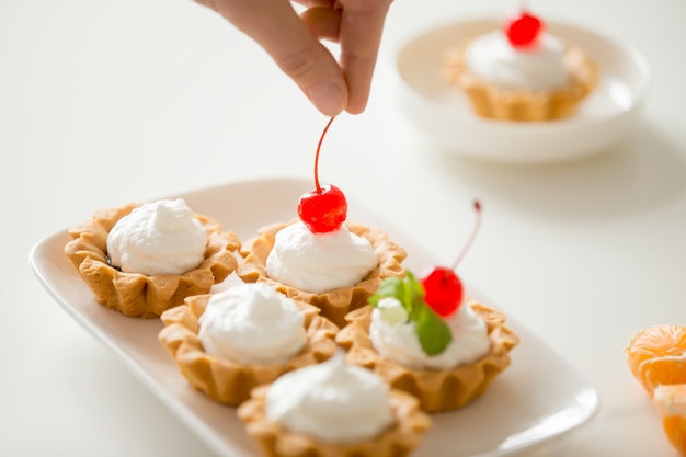 Gros plan de la décoration à la main de mini tartes à la crème avec de la cerise