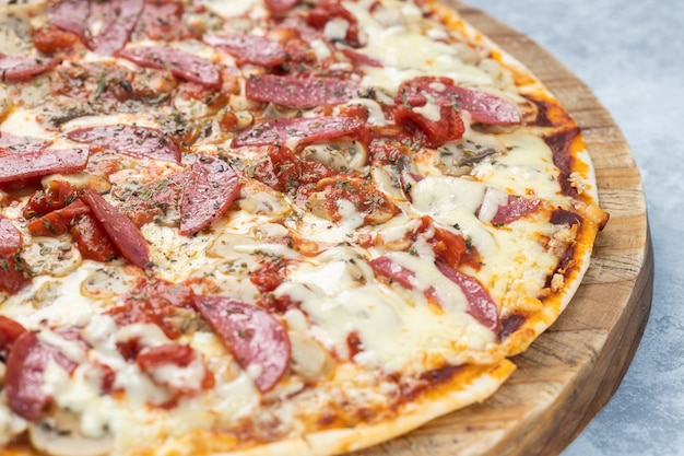 Gros plan d'une délicieuse pizza avec des saucisses tranchées et du fromage fondu sur une planche sous les lumières