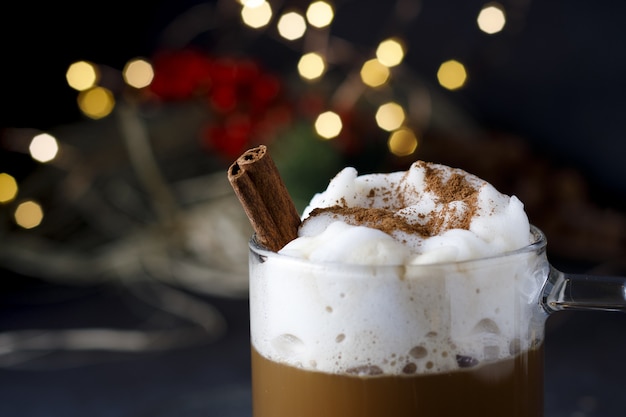 Gros plan d'un délicieux café de Noël avec de la cannelle et de la mousse, en face de lumières bokeh