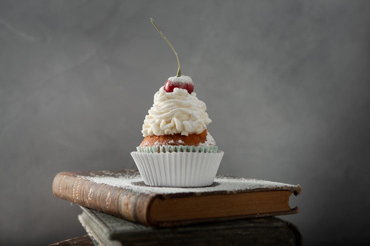 Photo gratuit gros plan sur un délicieux petit gâteau avec de la crème, du sucre en poudre et une cerise sur les livres