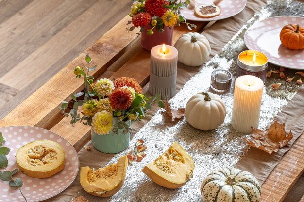 Gros plan sur les détails de la décoration chaleureuse d'une table à manger d'automne festive avec des citrouilles, des fleurs et des bougies.