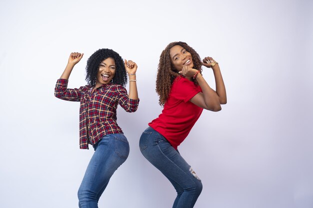 Gros plan de deux jeunes femmes noires excitées se sentir heureux et danser, devant un fond blanc