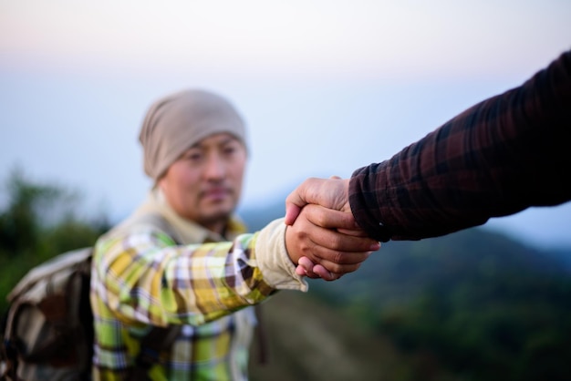 Gros plan de deux randonneurs masculins s'aidant mutuellement à gravir un paysage de montagne et de coucher de soleil Travail d'équipe et persévérance