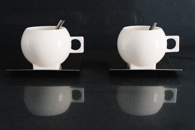 Photo gratuite gros plan de deux tasses blanches avec des cuillères à l'intérieur dans une cuisine carrelée sombre