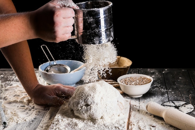 Gros plan du boulanger en passant la farine dans un tamis pour préparer la pâte