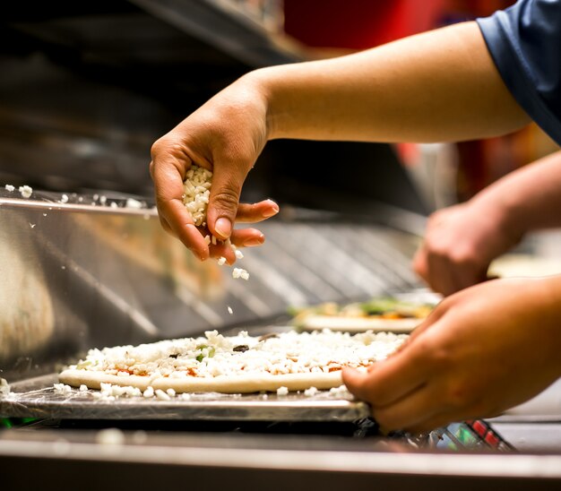 Gros plan du chef mettant du fromage sur la pâte à pizza recouverte de sauce tomate