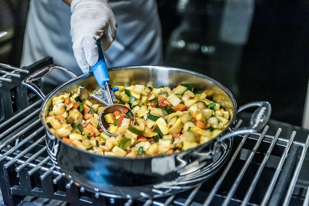 Gros plan du cuisinier préparer un plat avec des légumes dans une cuisinière en métal