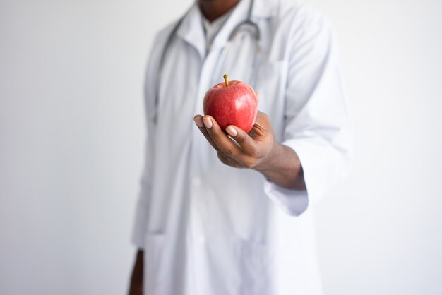 Gros plan du docteur masculin noir tenant et offrant la pomme rouge.