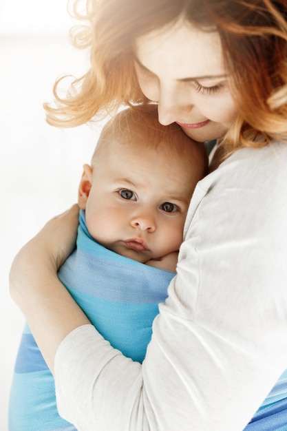 Gros plan du doux petit bébé avec ses grands yeux gris. Maman blottit son enfant avec tendresse et amour. Concept de famille.