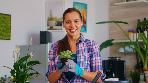 Gros plan du portrait femme souriante et tenant une fleur. Fleuriste replantant des fleurs dans un pot en céramique à l'aide d'une pelle, de gants, d'un sol fertile et de fleurs pour la décoration de la maison.