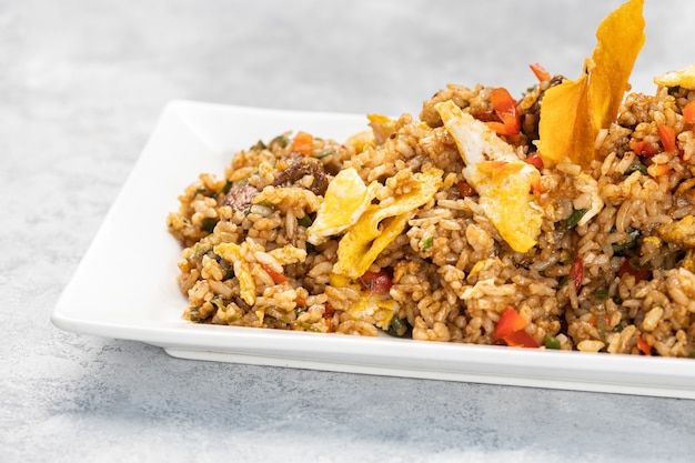 Gros plan du riz cuit épicé avec de la viande, des légumes et des frites dans une assiette sur la table