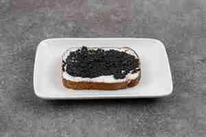 Photo gratuite gros plan du sandwich au caviar noir sur une plaque blanche sur une surface grise