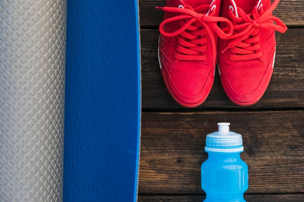 Gros plan du tapis d'exercice enroulé; chaussette et paire de chaussures de sport rouges sur une table en bois