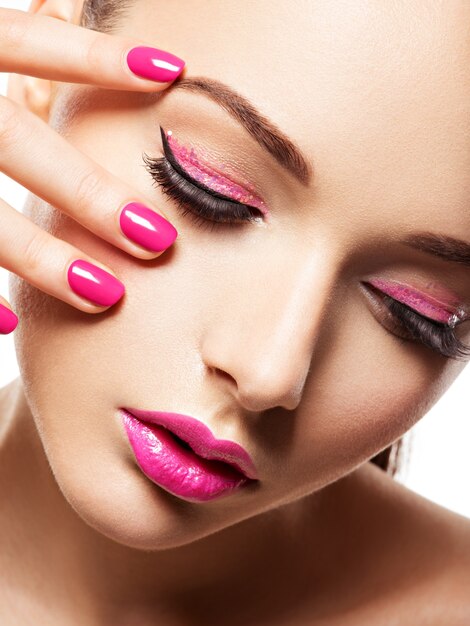 Gros plan du visage d'une belle fille avec du maquillage pour les yeux roses et des ongles rose vif. Mannequin posant sur un mur blanc